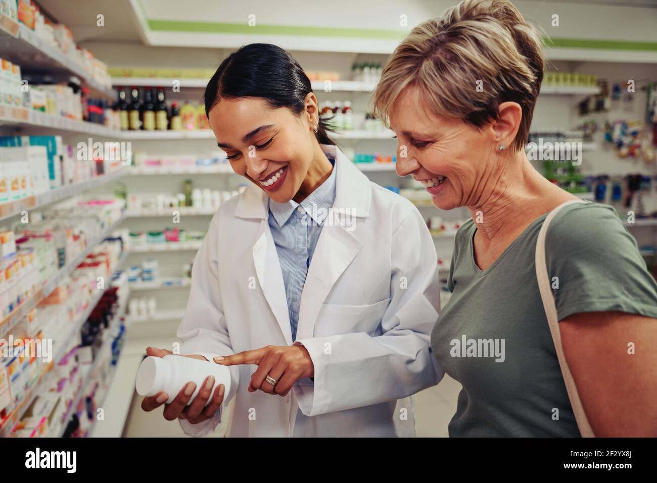 Lächelnder leitender Kunde mit Apotheker, der nach medizinischen Details zu sucht Flasche steht in der Nähe von Regalen Stockfoto