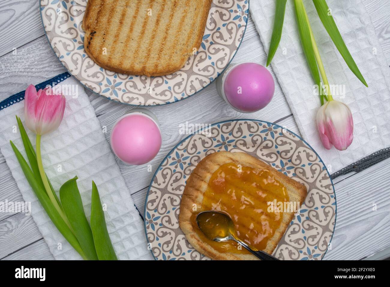 Rosafarbenes Osterei auf einem Frühstückstisch mit Marmelade und rosa weißen Tulpen und geröstetem Brot. Stockfoto