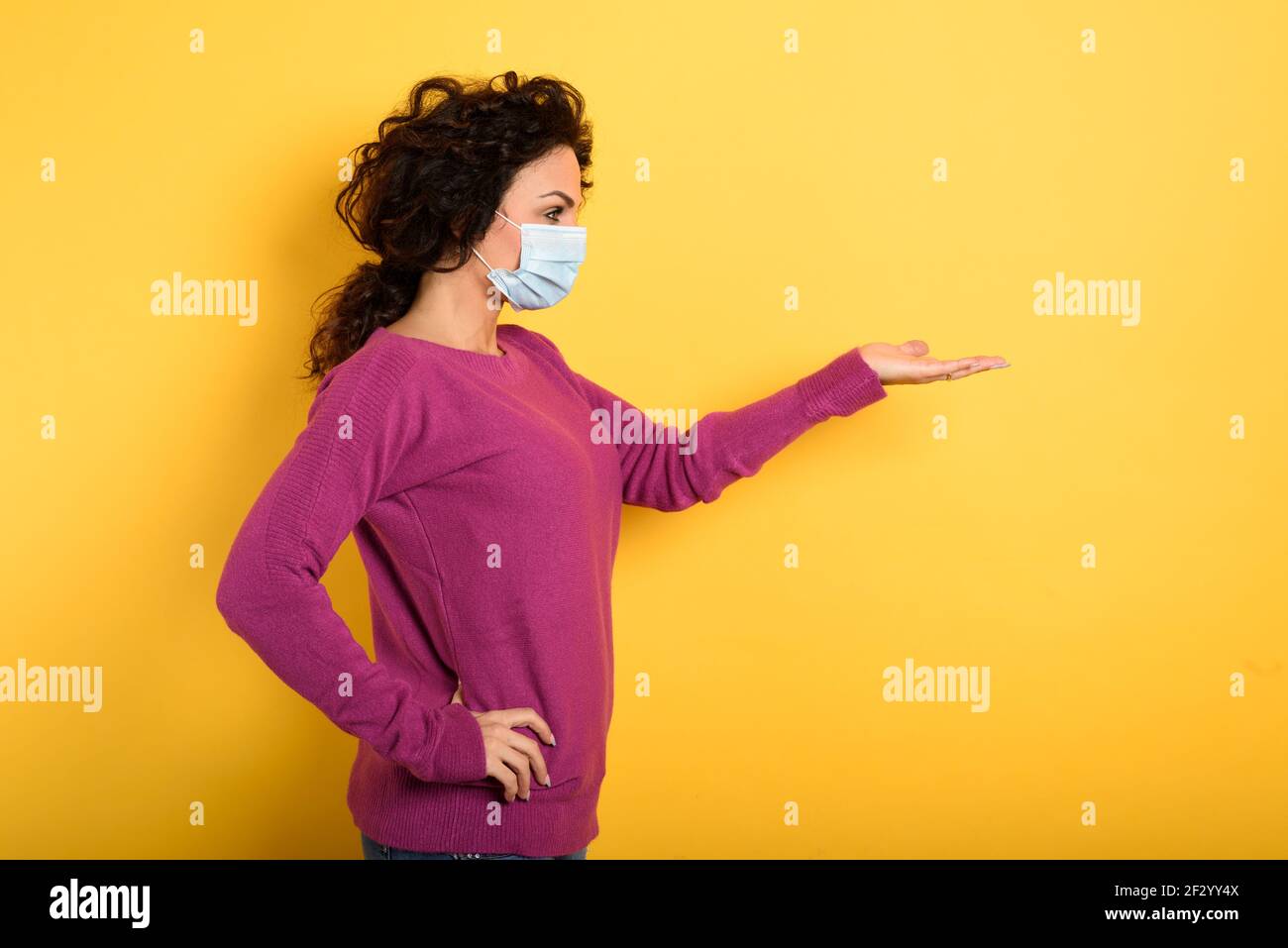 Nachdenkliche Frau mit Gesichtsmaske hält etwas in der Hand. Gelber Hintergrund Stockfoto