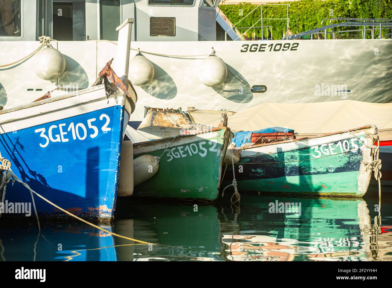 Traditionelle hölzerne Fischerboote werden neben einer modernen Motoryacht im Hafen von Camogli, Italien, vertäut. Die Farben der Boote spiegeln sich im Meer wider Stockfoto