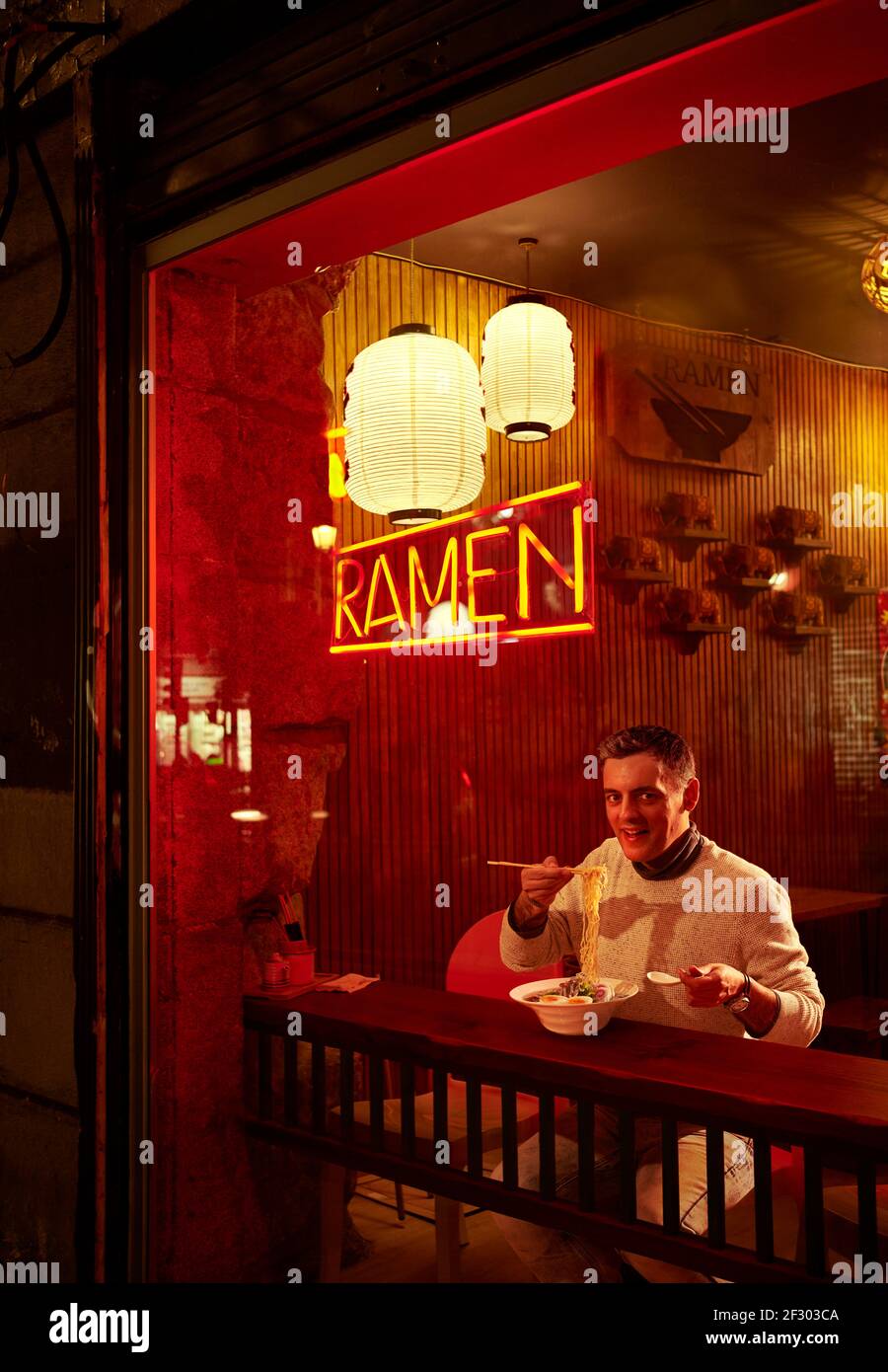 Ein europäischer Mann, der Ramen vor der Ladenfront eines japanischen Restaurants am Abend isst. Stockfoto