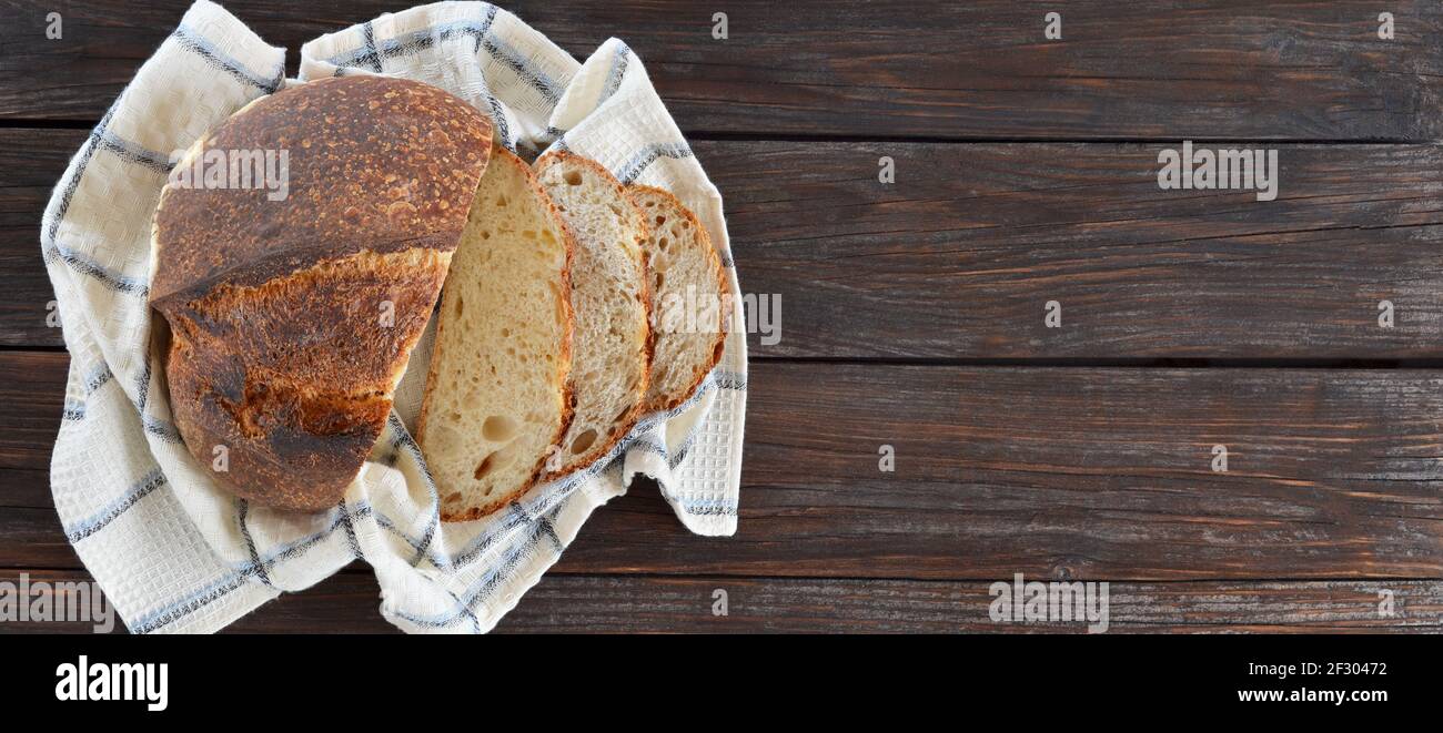 In Scheiben geschnittenes Brot mit einer knusprigen Kruste auf einem Küchentuch auf einem alten Holztisch mit Kopierfläche. Stockfoto