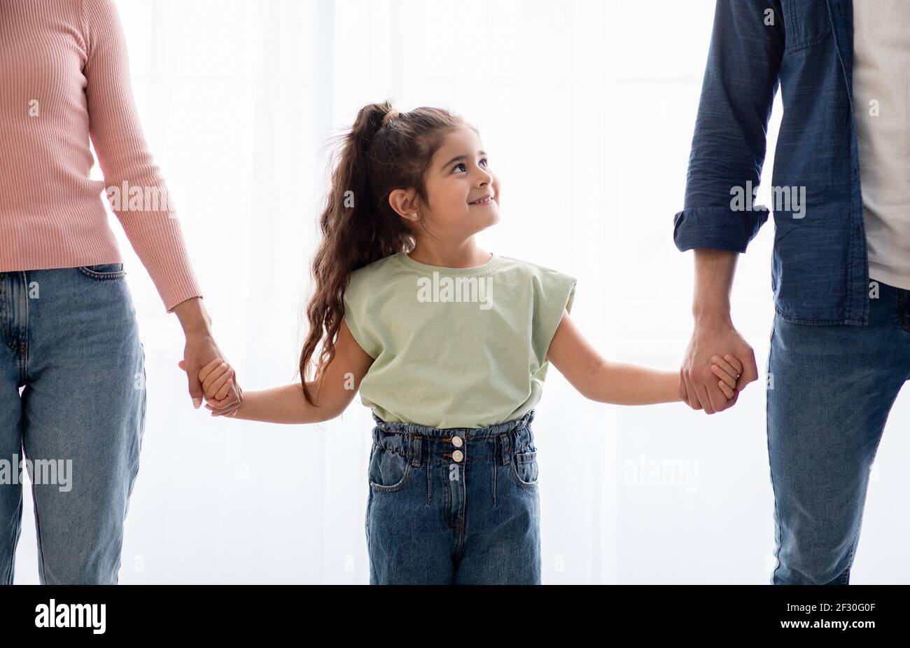 Adoptionskonzept. Liebenswert Kleines Mädchen Halten Hände Mit Unkenntlich Mama Und Papa Stockfoto