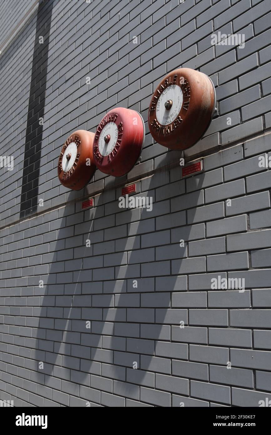 Nahaufnahme von drei roten Sprinkleralarmen, die an einem montiert sind Graue Ziegelwand Stockfoto