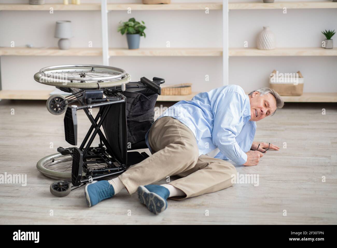 Älterer Mann mit körperlicher Behinderung, der nach einem Sturz auf dem Boden liegt Unten von seinem Rollstuhl zu Hause Stockfoto