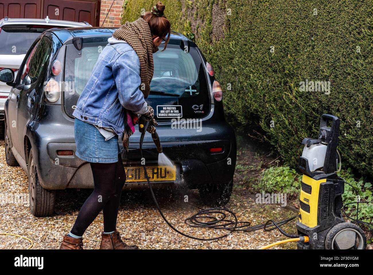 Frau, die ein Auto mit einem Hochdruckreiniger reinigt, Alresford, Hampshire, Großbritannien Stockfoto
