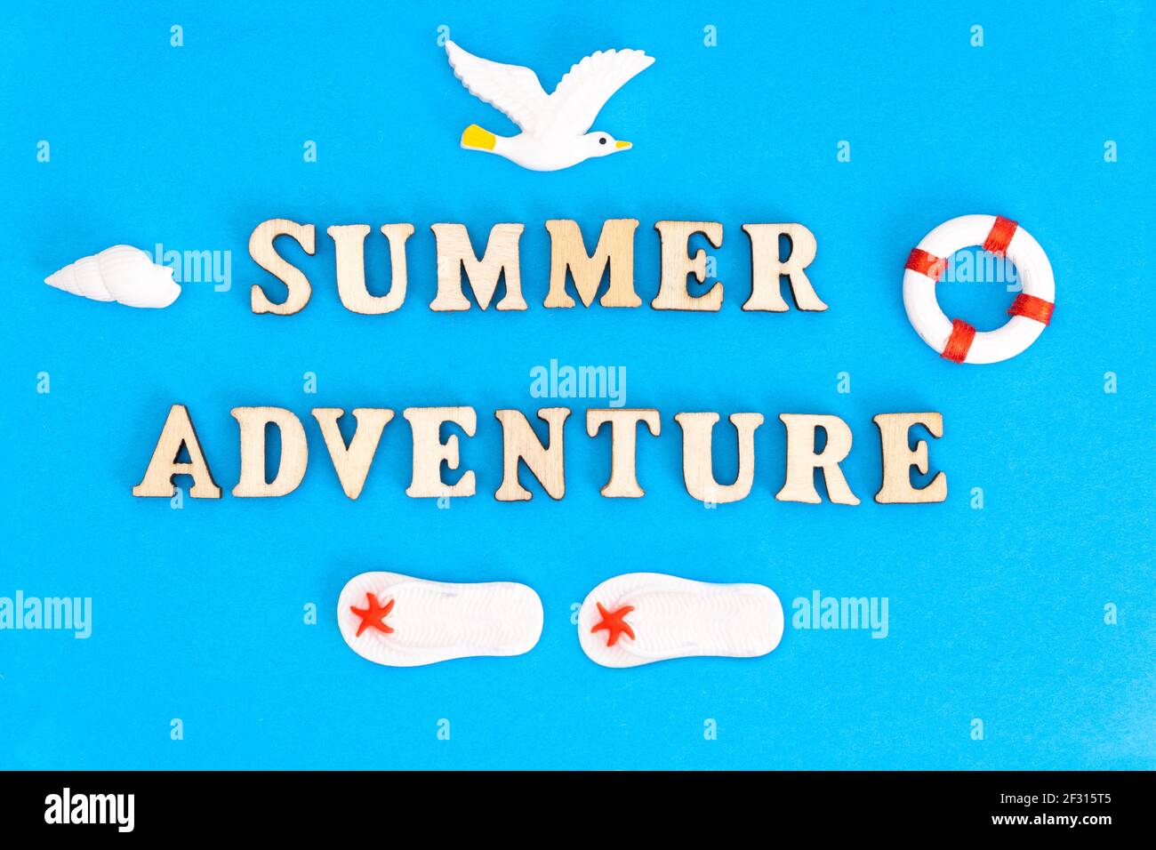 Kreative Sommerurlaub Komposition: Schriftzug SOMMER ABENTEUER aus Holzfiguren auf blauem Hintergrund zusammen mit Spielzeug Möwe, Flip ANGEORDNET Stockfoto