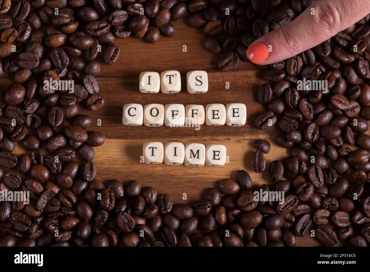 Es ist Kaffeezeit mit einem Holzwürfel Buchstaben und eine Frau Hand mit  einer Kaffeebohne und Kaffee rund um auf einem Holztisch. Guten Morgen  Stockfotografie - Alamy