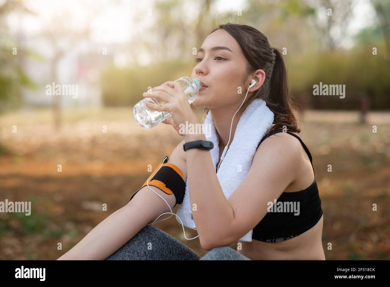 Die junge Sportlerin macht eine Pause, trinkt Wasser und läuft an einem heißen Tag. Stockfoto