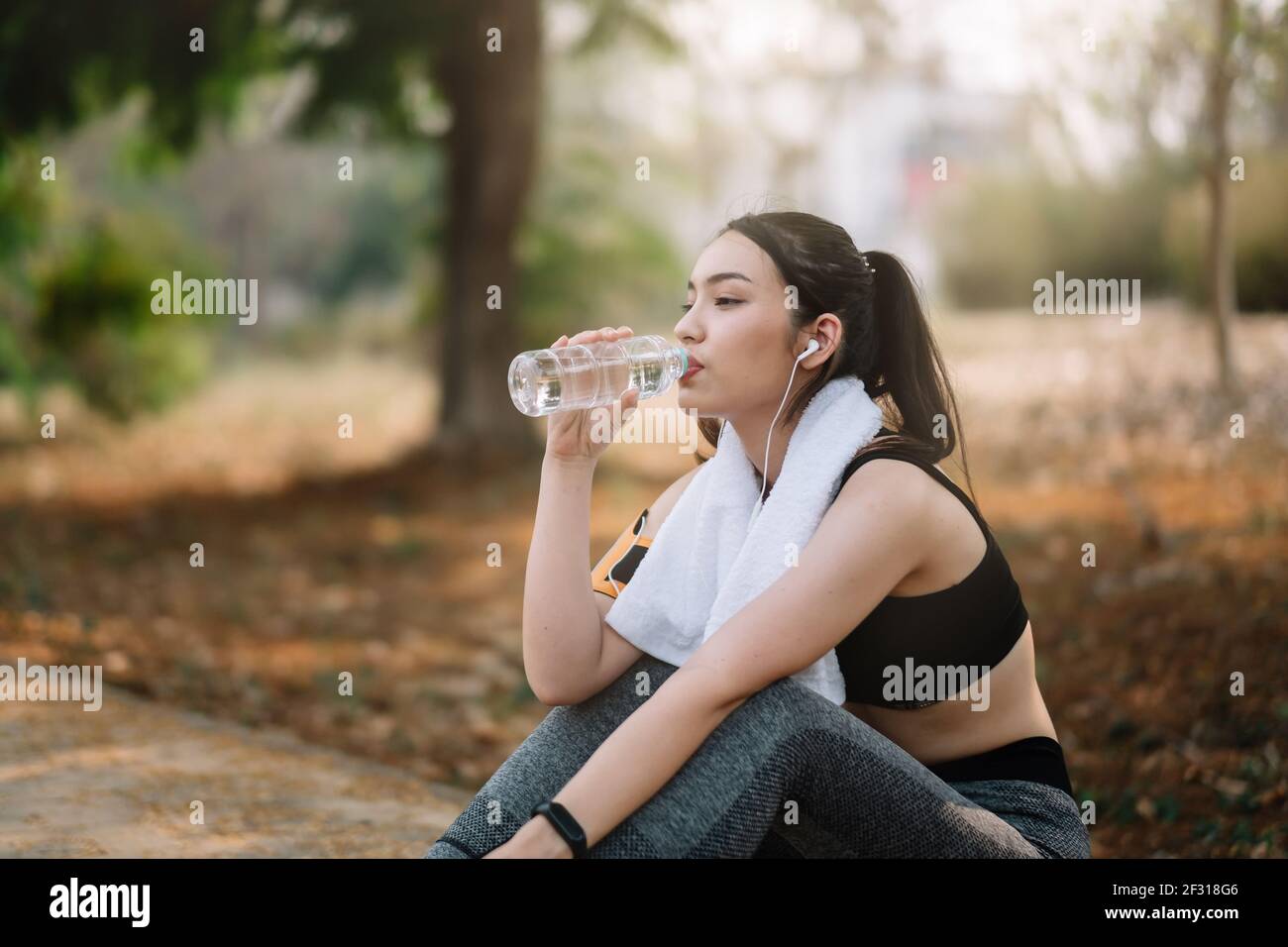 Die junge Sportlerin macht eine Pause, trinkt Wasser und läuft an einem heißen Tag. Stockfoto