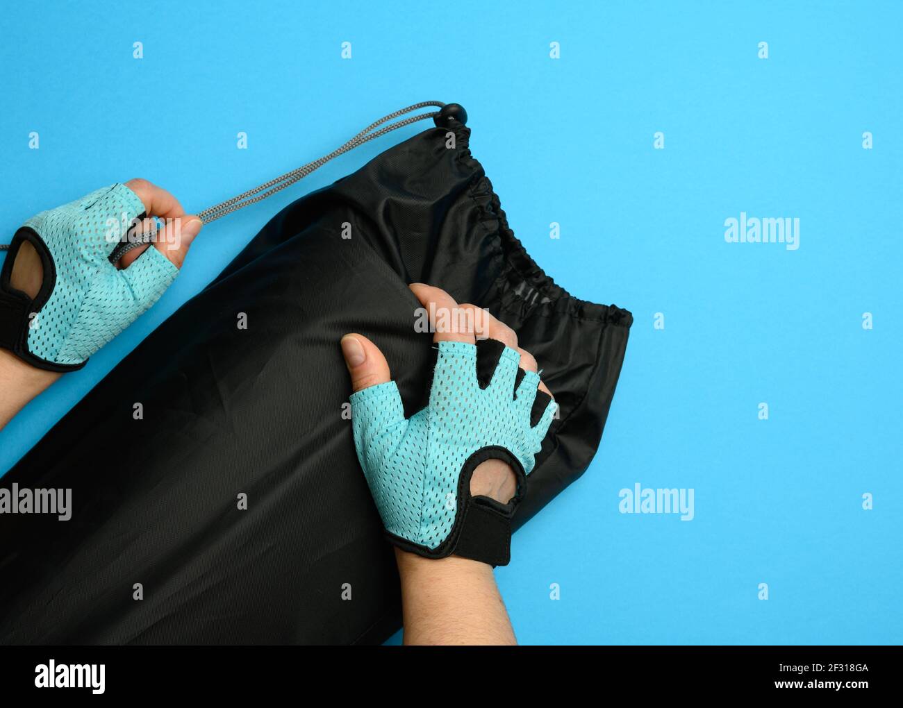Weibliche Hände in Handschuhen halten eine Tasche mit einem verdrehten Sportmatte auf blauem Hintergrund Stockfoto