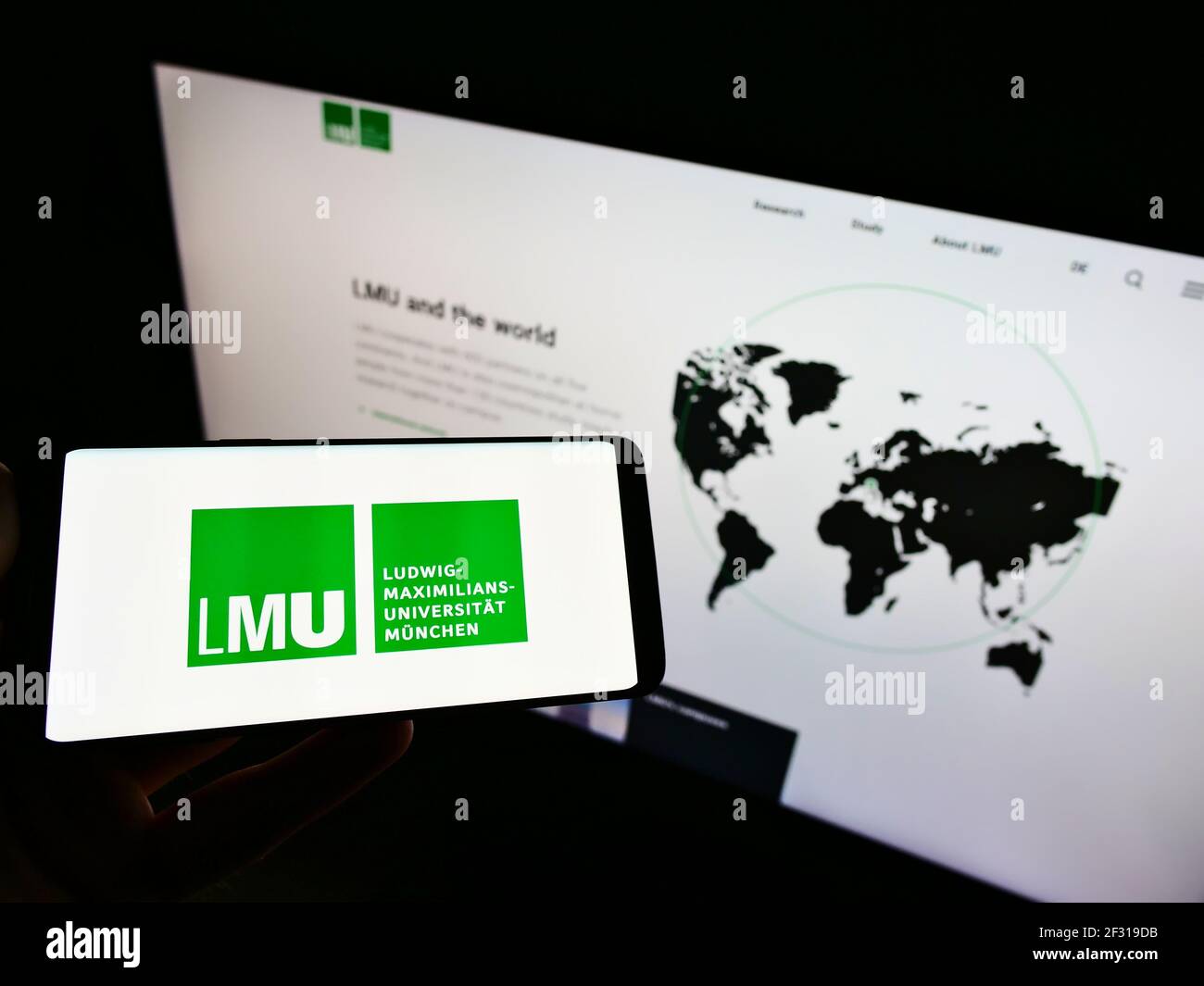 Person, die Smartphone mit Logo der Ludwig-Maximilians-Universität München auf dem Bildschirm vor der Website hält. Konzentrieren Sie sich auf die Telefonanzeige. Nicht modifiziertes Foto. Stockfoto