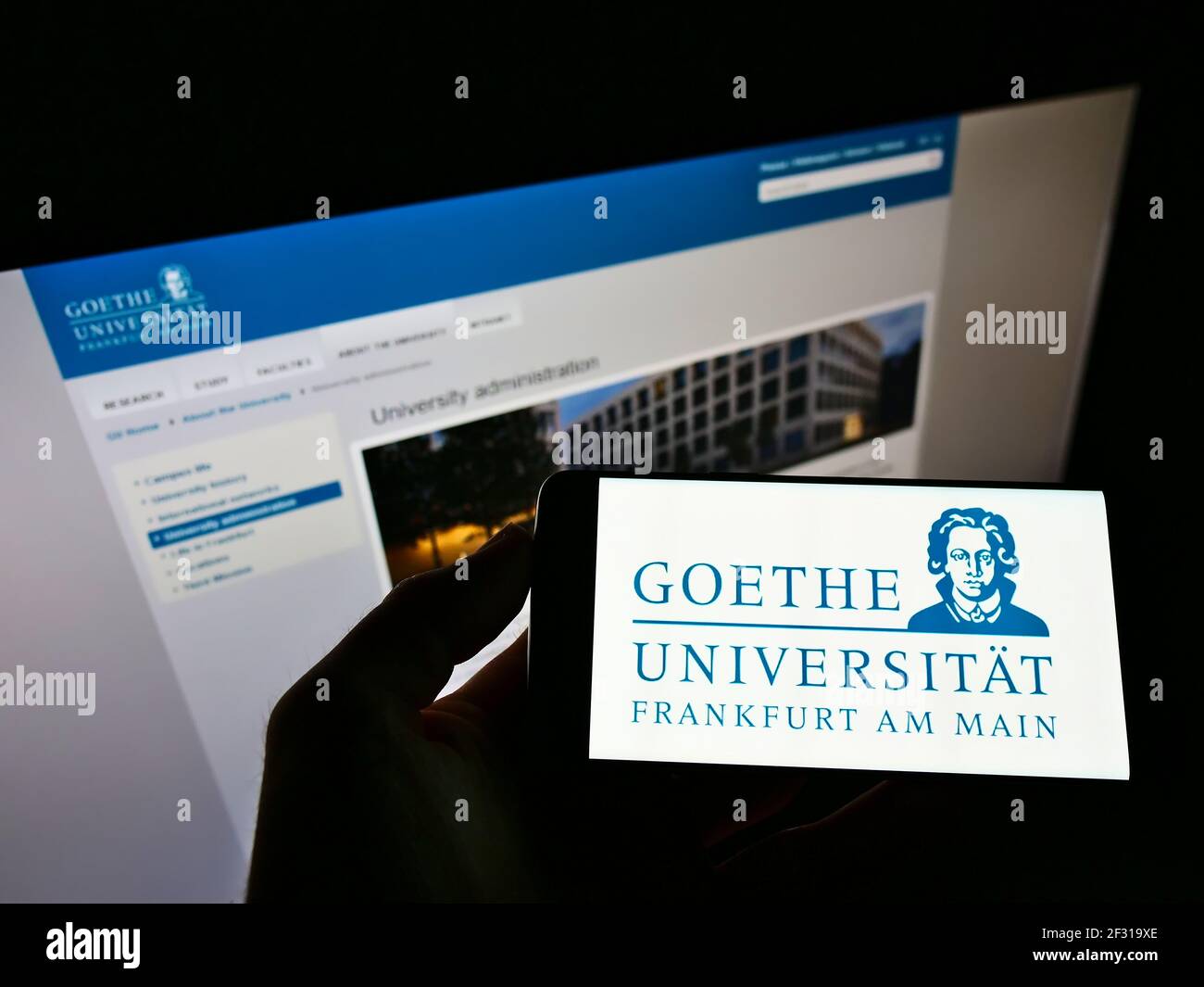 Person, die Smartphone mit Logo der Goethe-Universität Frankfurt am Main auf dem Bildschirm vor der Website hält. Konzentrieren Sie sich auf die Telefonanzeige. Stockfoto