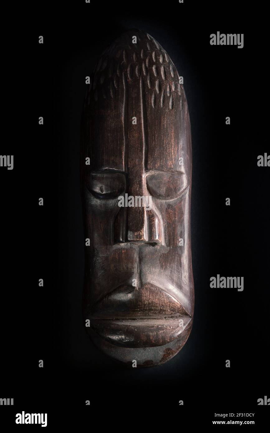 Holzskulptur des menschlichen Gesichts im afrikanischen Stil. Holzschnitzerei aus dunklem Holz. Afrikanische Stammesmaske isoliert auf schwarzem Hintergrund. Kunst und Kultur des Afrikanischen Stockfoto
