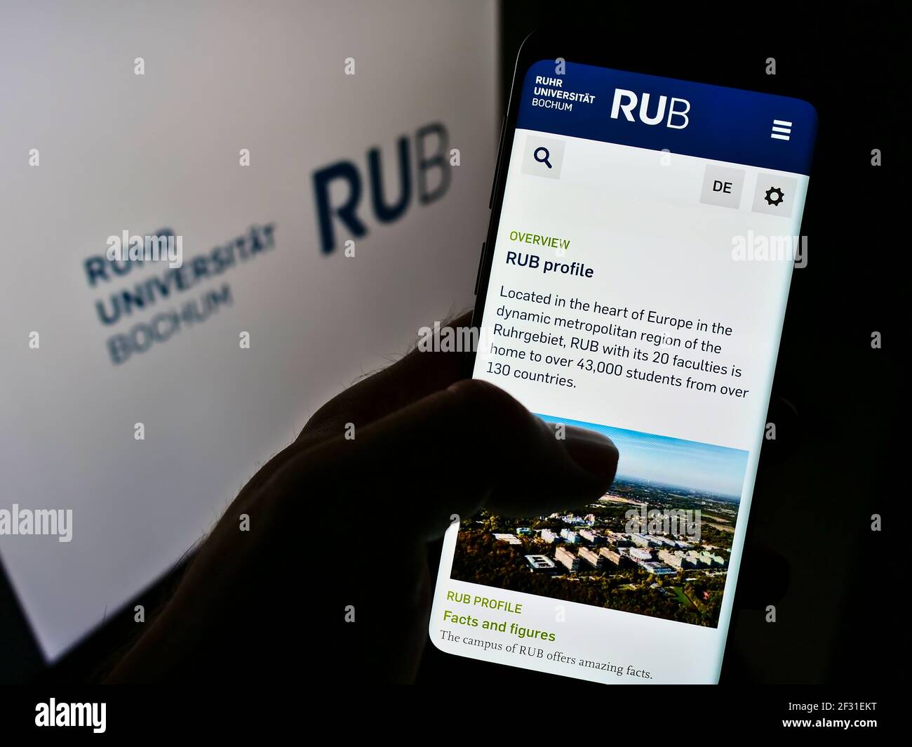 Person, die Mobiltelefon mit der Webseite der Ruhr-Universität Bochum (RUB) auf dem Bildschirm vor dem Logo hält. Konzentrieren Sie sich auf die Mitte des Telefondisplays. Stockfoto