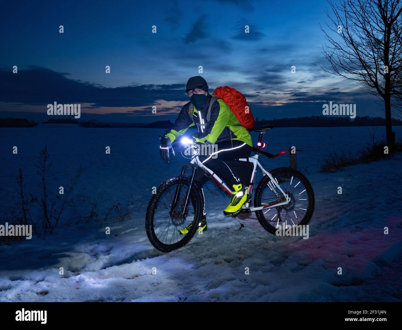 Guy Radfahrer sitzt auf einem MTB während einer Nachtfahrt. Stadtpark und leichter Schneefall im Nebel. Stockfoto