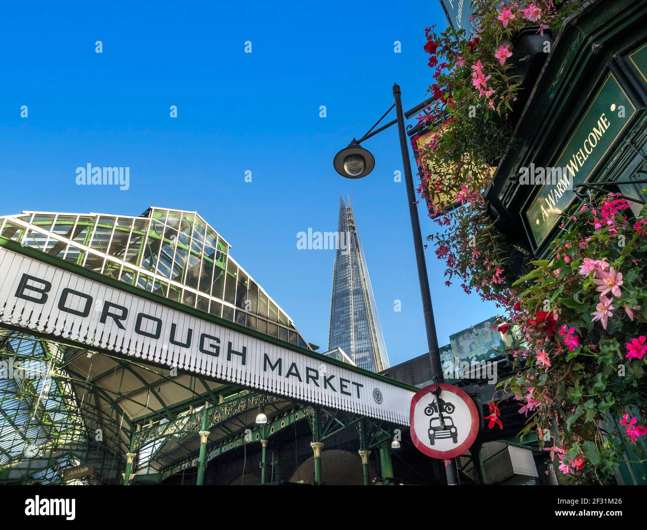 Borough Market Schild an der Londoner Außenfassade mit Blumen rund um den 'Market Porter Pub' mit einem 'herzlichen Willkommen' Schild über dem Eingang. LTN Low Traffic Neighbourhood LTN Straßenschild an der Ampel. Außenansicht des internationalen Marktes mit The Shard hinter der London Bridge Southwark London UK Stockfoto