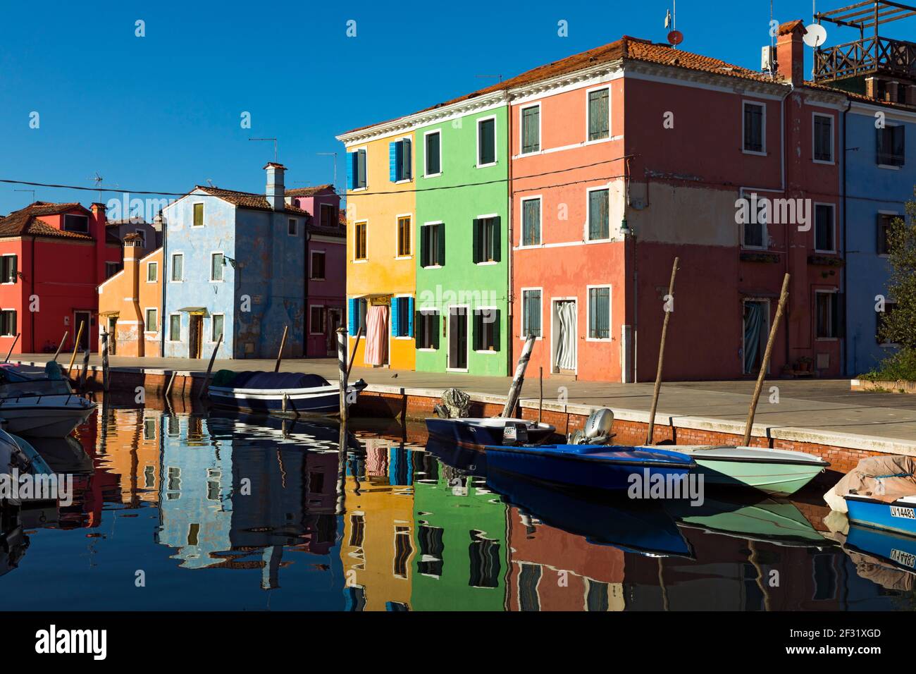Italien, Venedig, Burano. Farbenfrohe Gebäude, die einst Lagerhäuser waren, spiegeln sich in einem Kanal wider Stockfoto