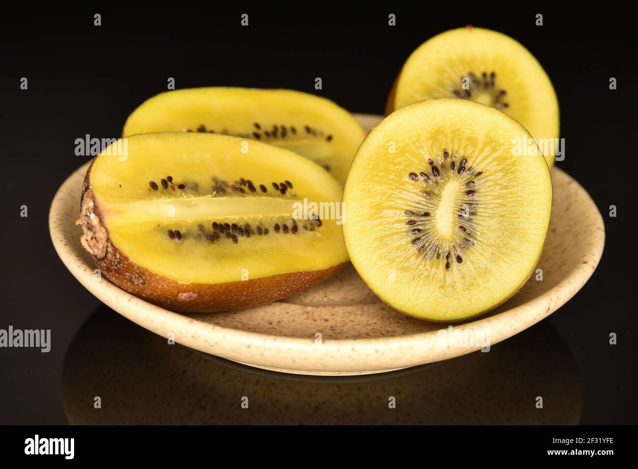 Vier Hälften von reifen Bio süß köstliche goldene Kiwi, in Längs-und Querschnitt, auf einer hellen Keramik-Untertasse, close-up, auf schwarzem Hintergrund Stockfoto