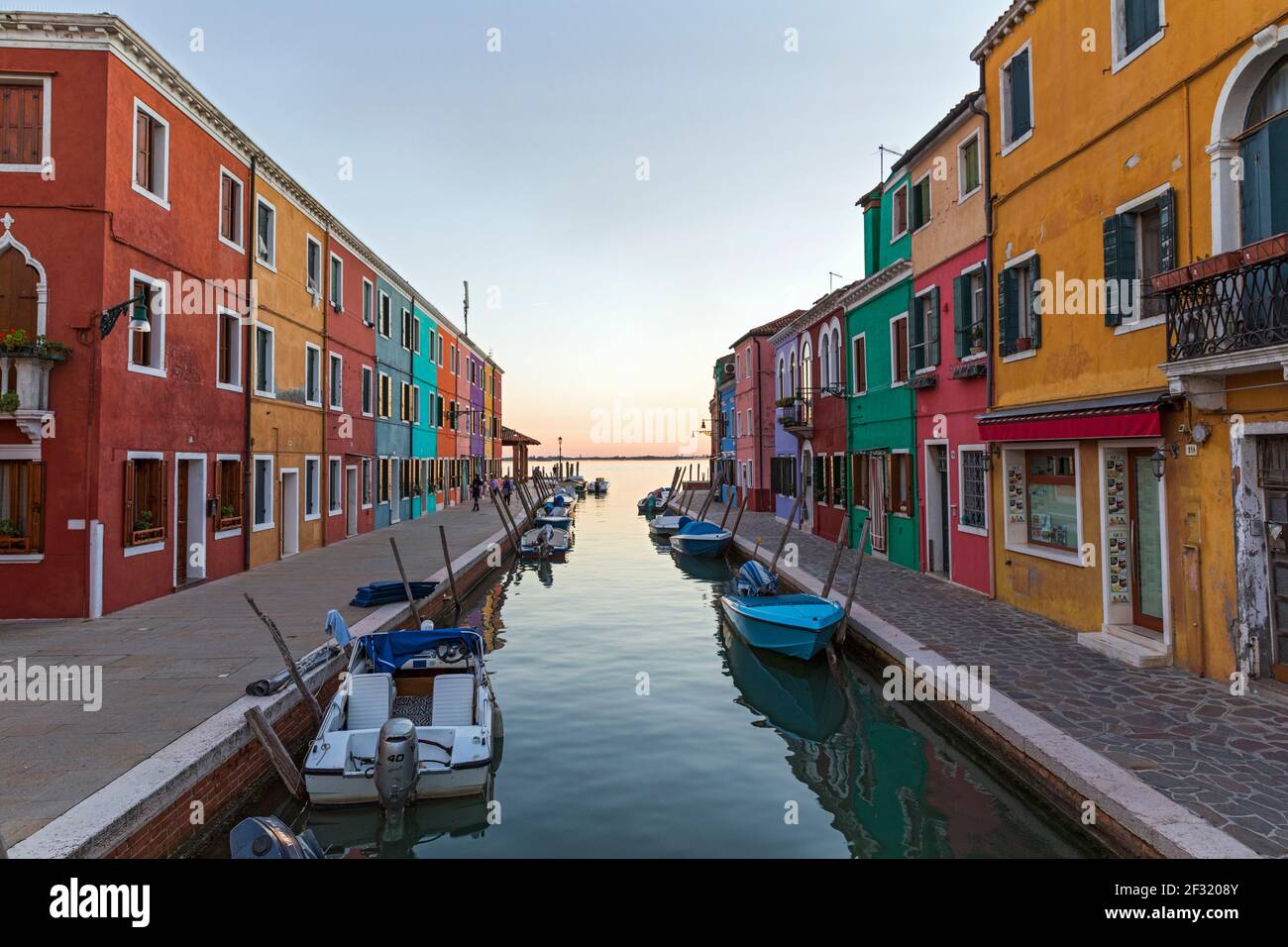Die venezianische Insel Burano, Boote auf einem Kanal, bunte Häuser und Geschäfte in der Dämmerung mit Menschen auf den Gehwegen. Stockfoto