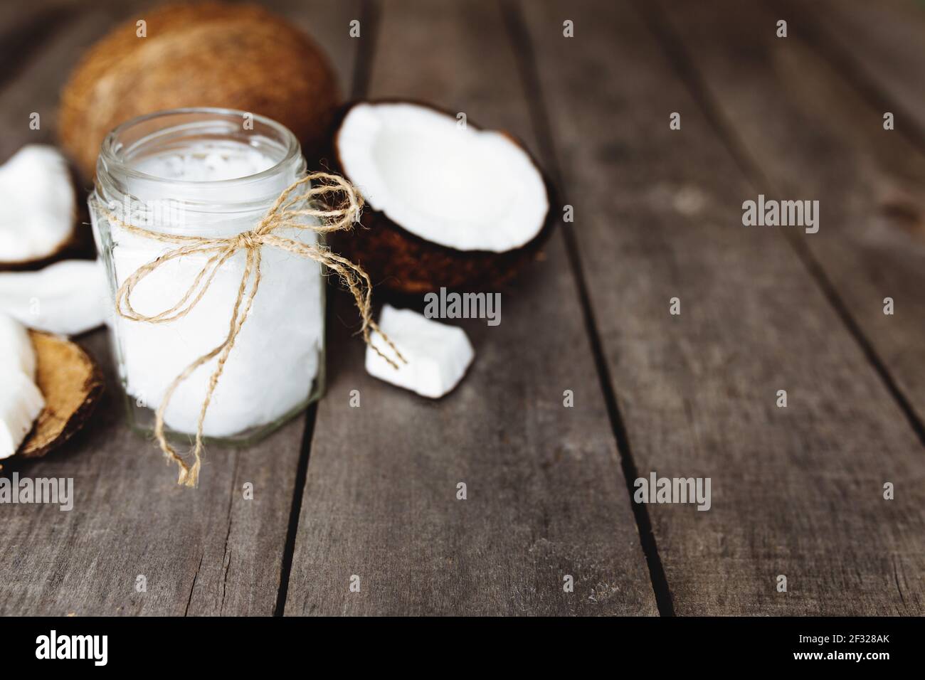 Zerbrochene Kokosnüsse auf grauem Holzhintergrund mit Glas rohem Bio-Kokosöl extra vergine. Weißes Kokosnusspulpe. Hochwertige Fotos Stockfoto