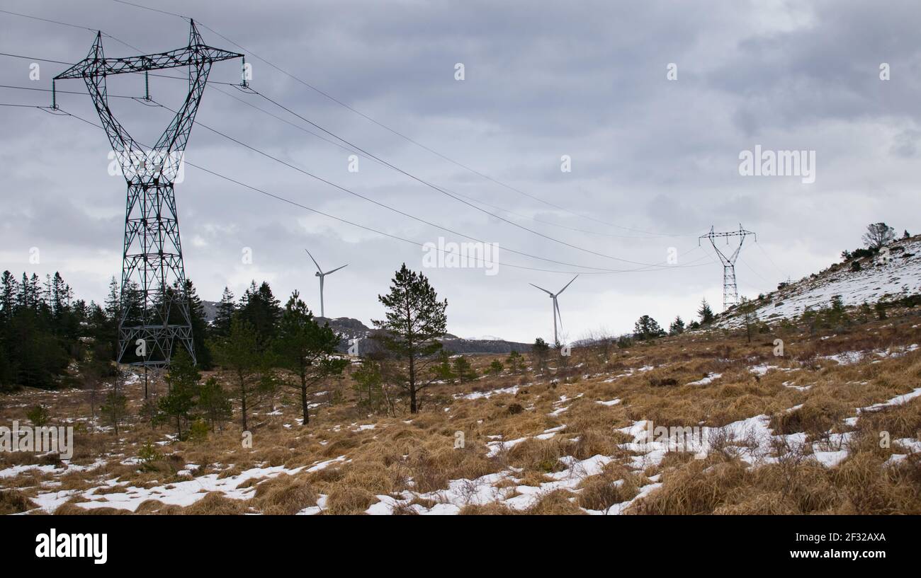 Windmühle neben Stromleitungen während der Winterzeit in Norwegen. Konzept für saubere Energie Stockfoto