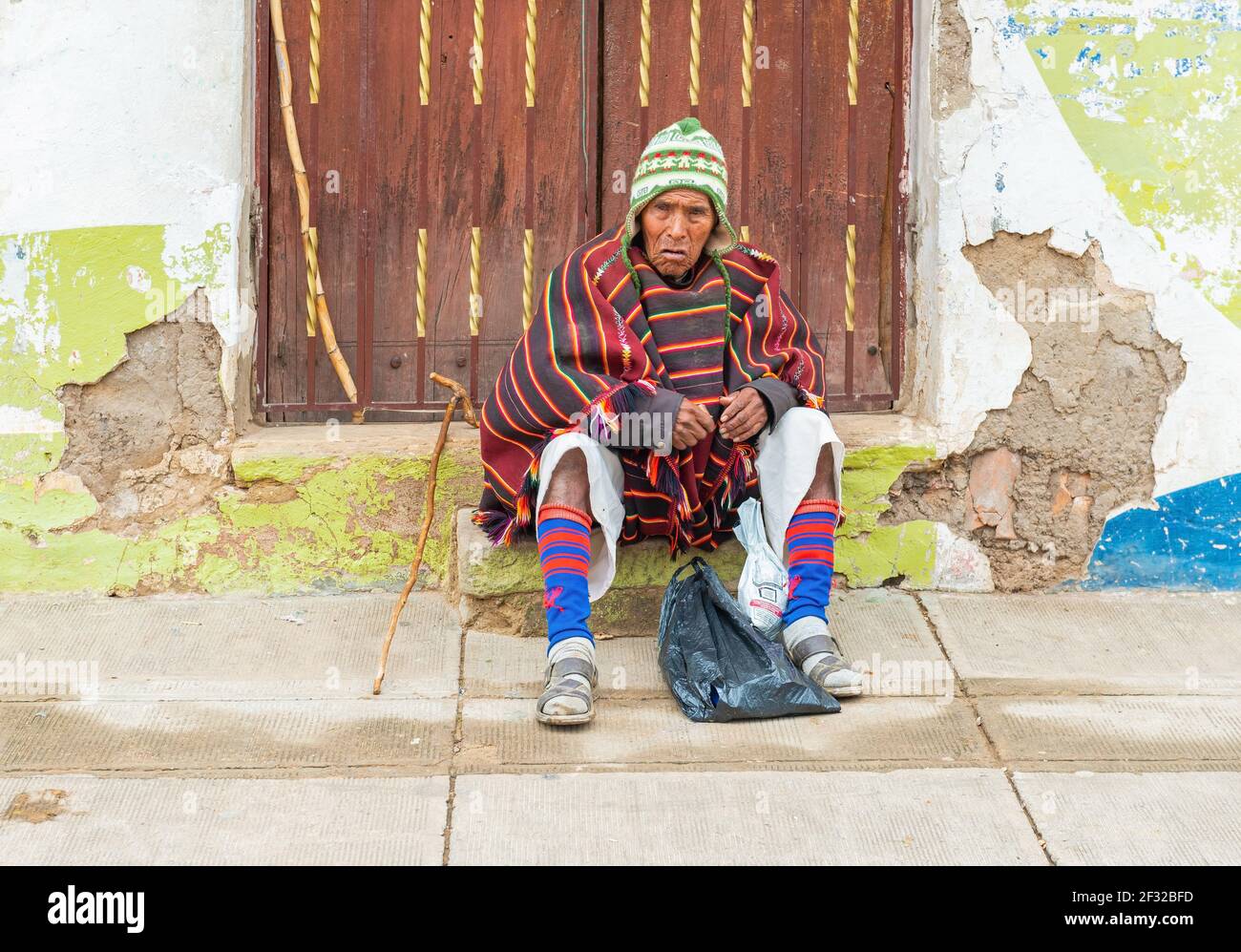 Indigener Tarabuco Mann in traditioneller Kleidung sitzt vor einer Holztür, Tarabuco Stadt, Sucre Department, Bolivien. Stockfoto