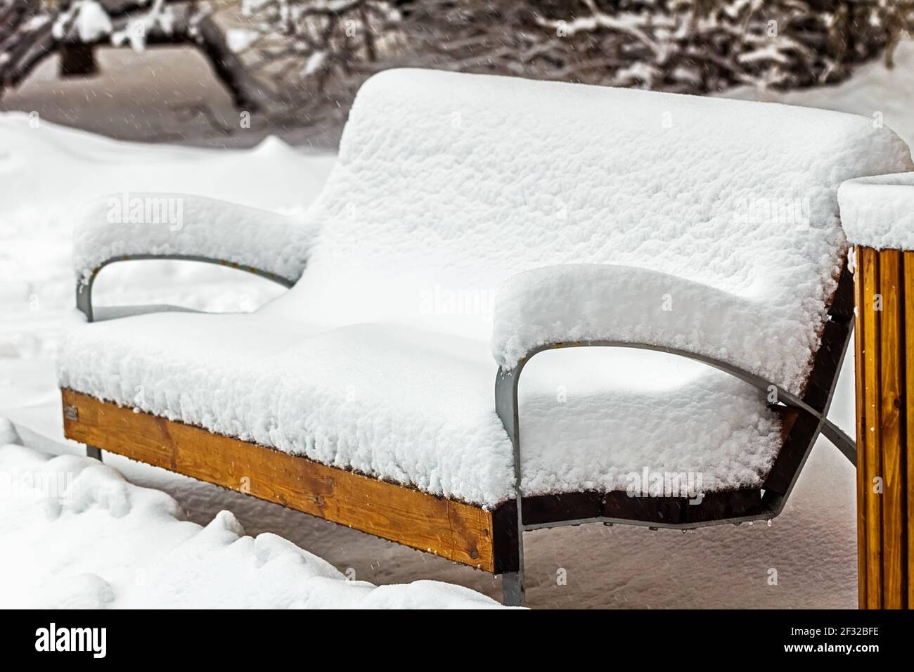 Echte hübsche Holzbank, die tagsüber komplett mit Schnee bedeckt ist Stockfoto