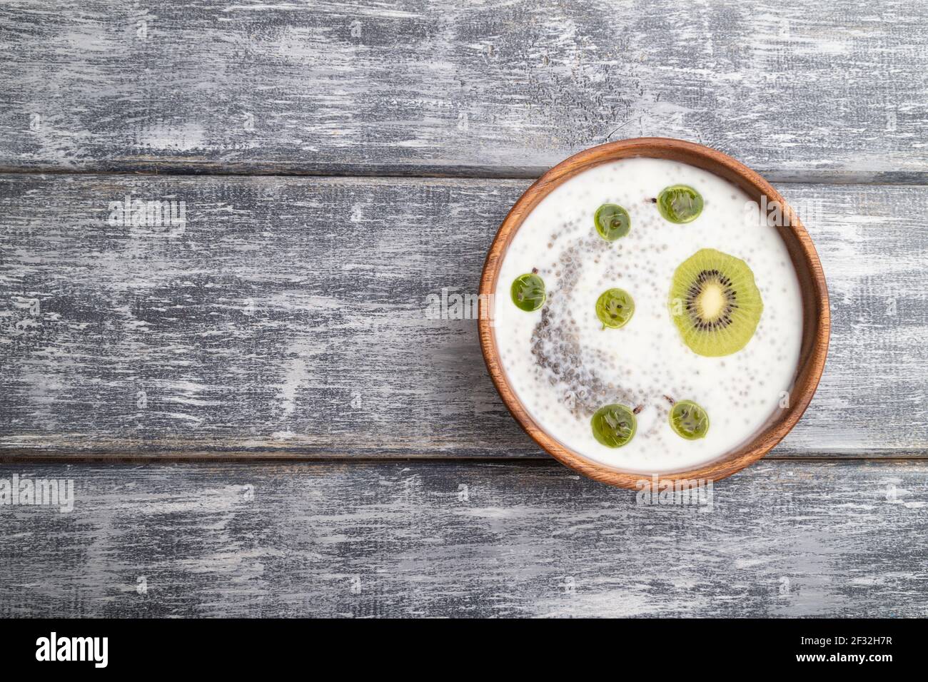 Joghurt mit Kiwi, Stachelbeere, Chia und Mandeln in Holzschüssel auf grauem Holzgrund. Draufsicht, flaches Lay, Kopierraum. Stockfoto