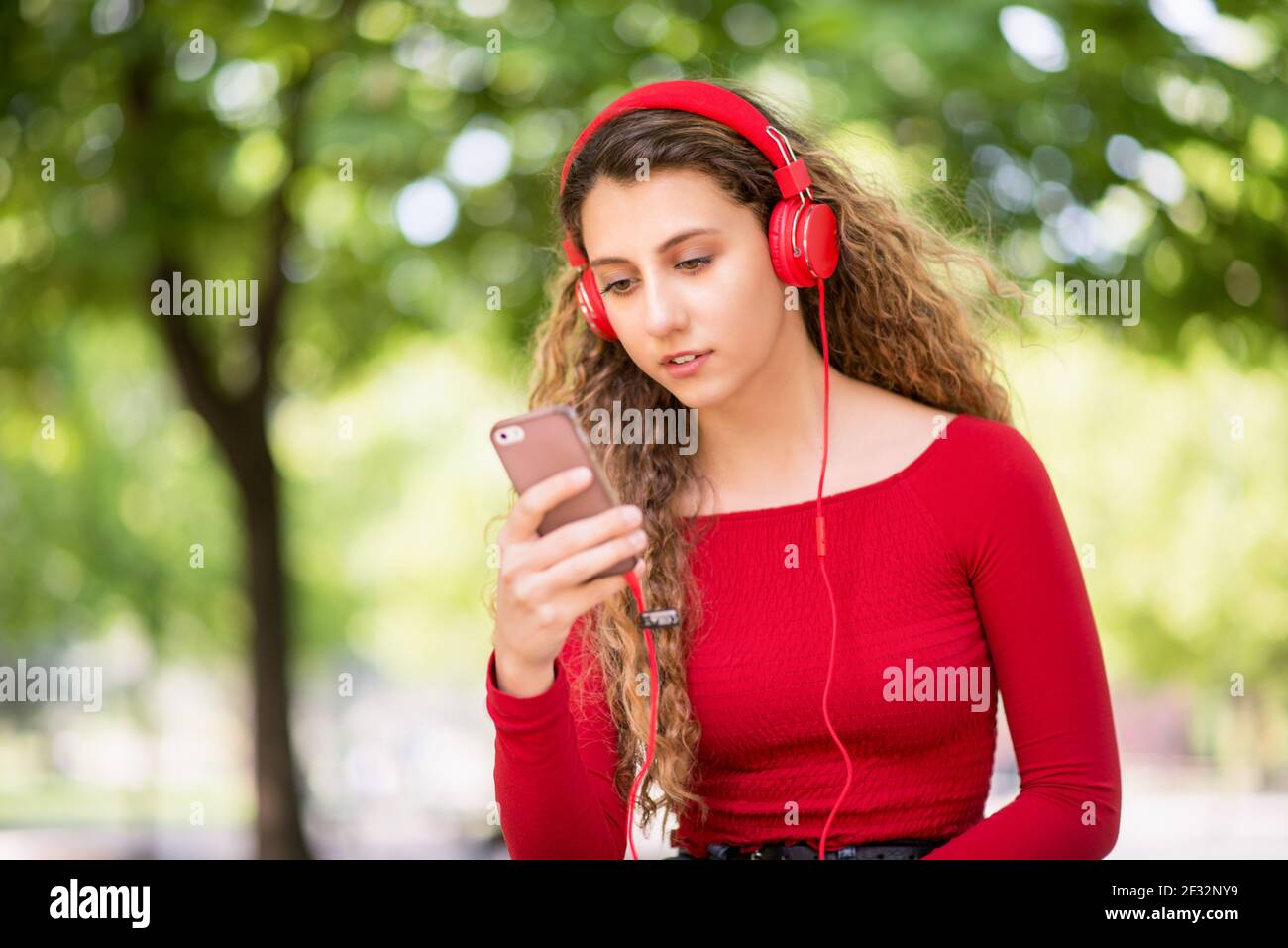Rot gekleideter Teenager, der in einem Park Musik vom Telefon hört Stockfoto