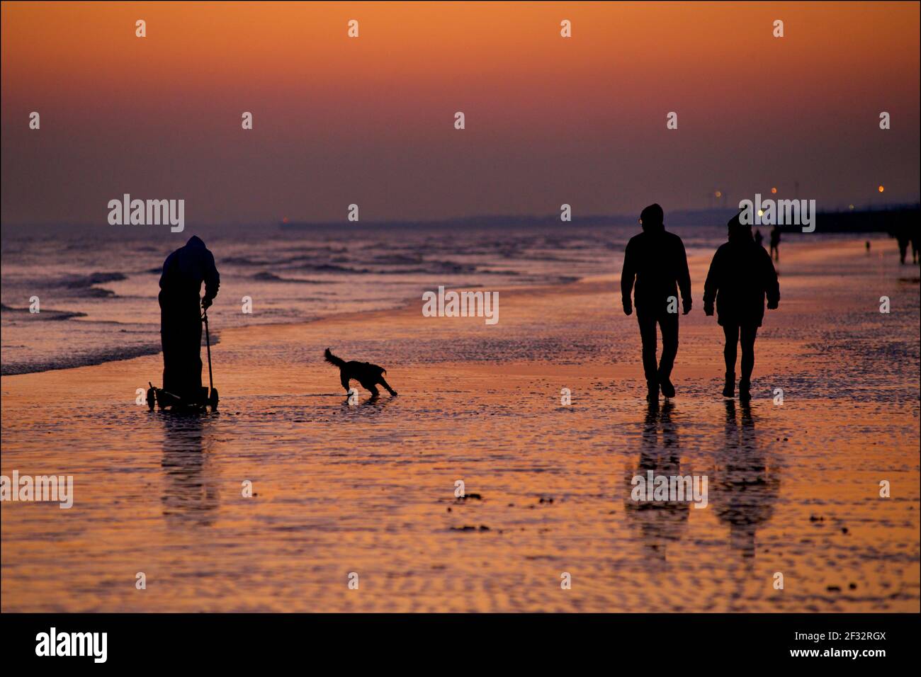 Brighton und Hove Beach bei Ebbe und Blick nach Westen. Silhouetten von Menschen, die bei Sonnenuntergang am Ufer entlang gehen. Fischer sammeln Würmer für Fischköder. Sussex, England. Stockfoto