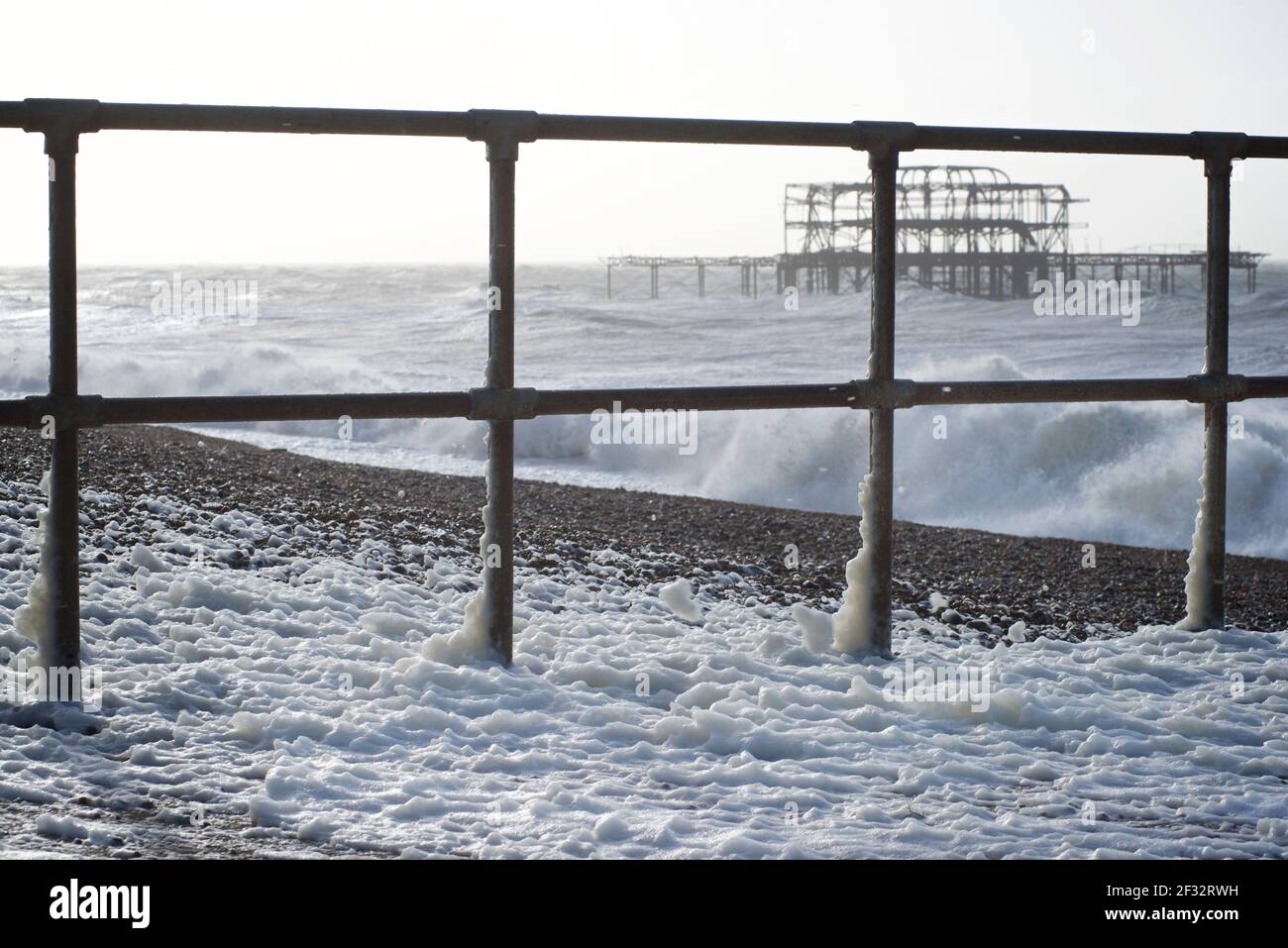 Geländer, die zu einem Groyne an der Strandpromenade von Brighton führen, mit den Ruinen des West Pier im Hintergrund in einem Sturm, mit den von der stürmischen See, Brighton, aufgeschäumten Nähten. East Sussex, England Stockfoto
