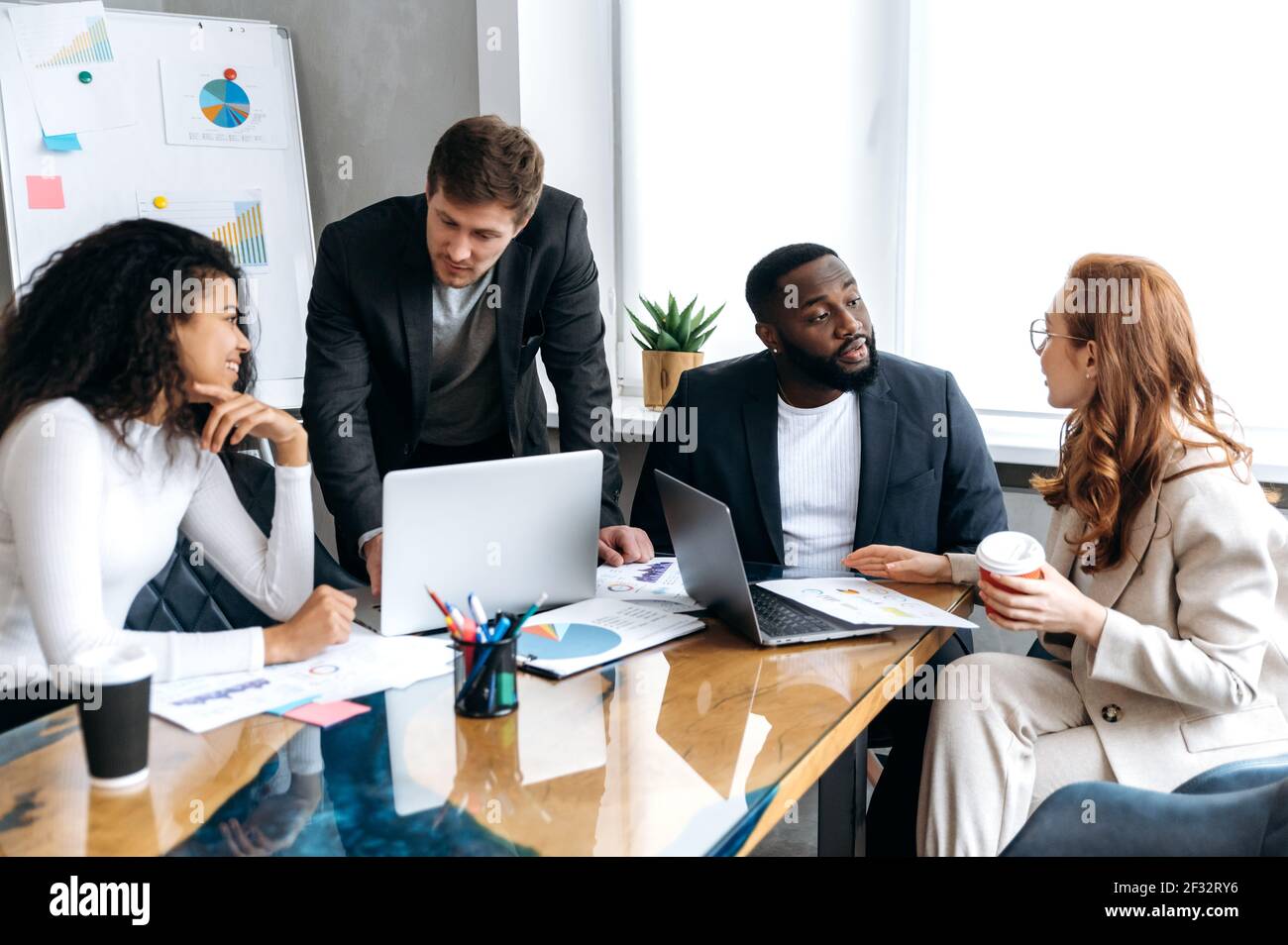 Einflussreiches Business-Team in modernen Büro auf Briefing, Arbeit an neuen Projekt. Erfolgreiche männliche und weibliche Mitarbeiter diskutieren Ideen, lernen Finanzgraphen, mit Laptop Stockfoto