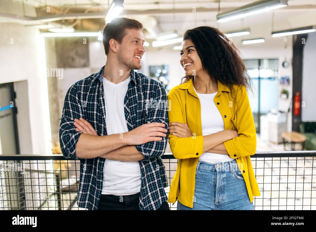 Portrait erfolgreicher stilvoller Freunde Kollegen oder Studenten, die sich gegenseitig lächeln. Glückliche junge Erwachsene multirassische Menschen stehen in modernen Büro mit Kreuzhände, Partnerschaften Konzept Stockfoto