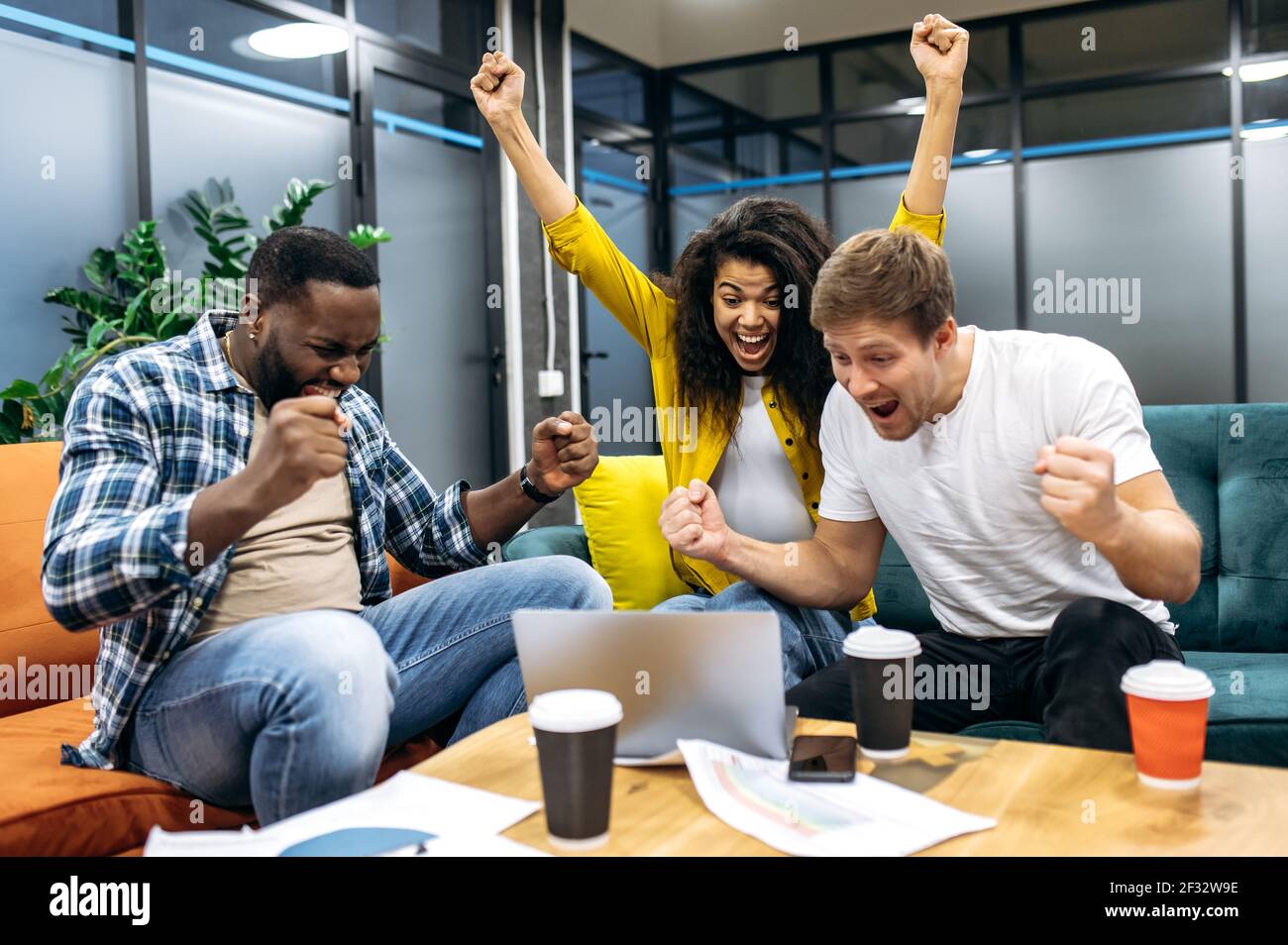 Überglücklich fühlen sich Mitarbeiter oder Studenten im Büro euphorisch, blicken auf den Laptop-Bildschirm und schreien. Aufgeregt männlich und weiblich Bestehen wichtige Prüfungen oder einen großen Gewinn aus Unternehmensprojekt Stockfoto