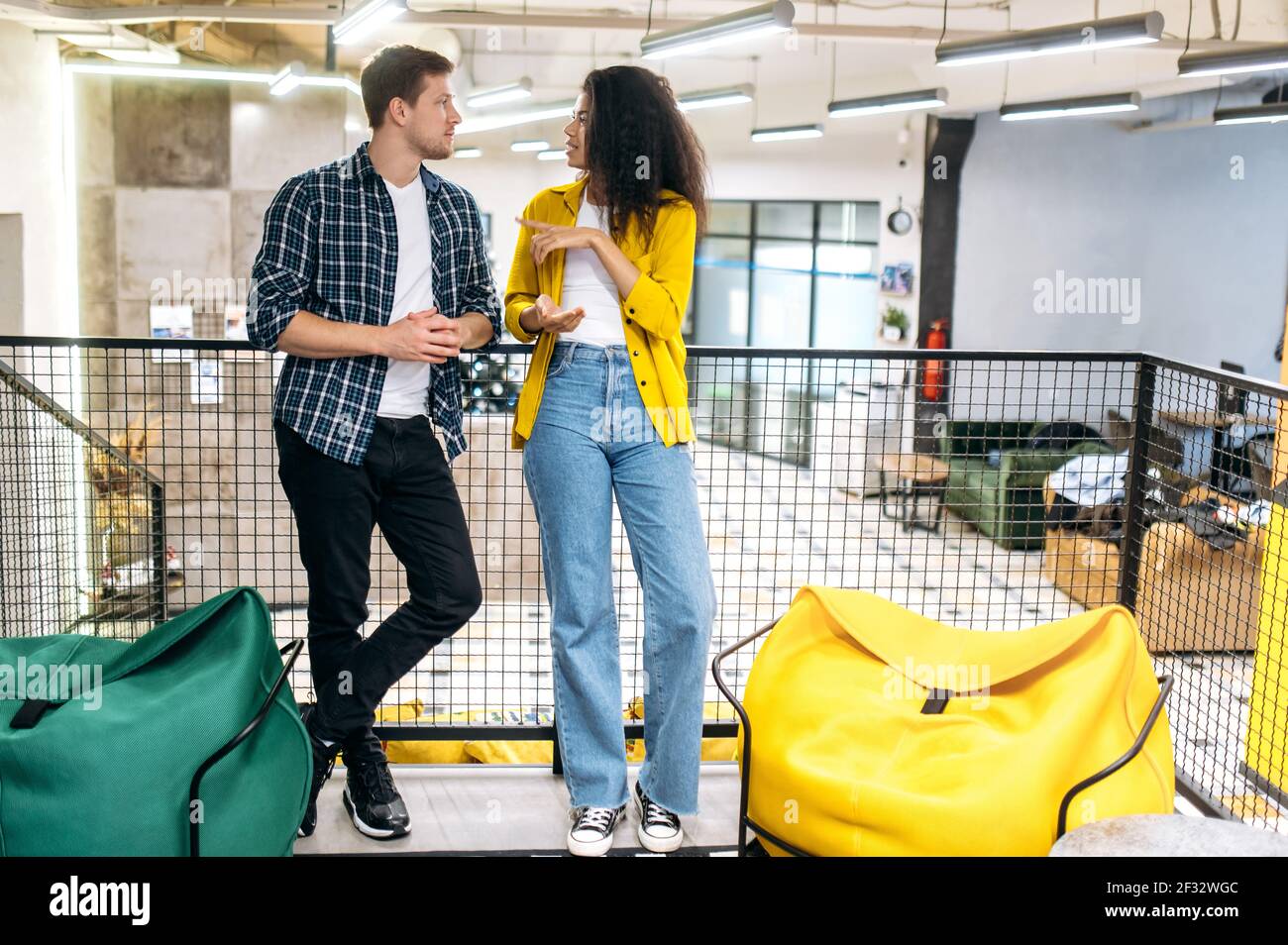 Stilvolle Freunde Kollegen oder Studenten, die ein Gespräch führen, stehen im modernen Büro. Junge Erwachsene multiethnische Kollegen sprechen über Unternehmensprojekt, diskutieren Arbeits- oder Studienfragen Stockfoto