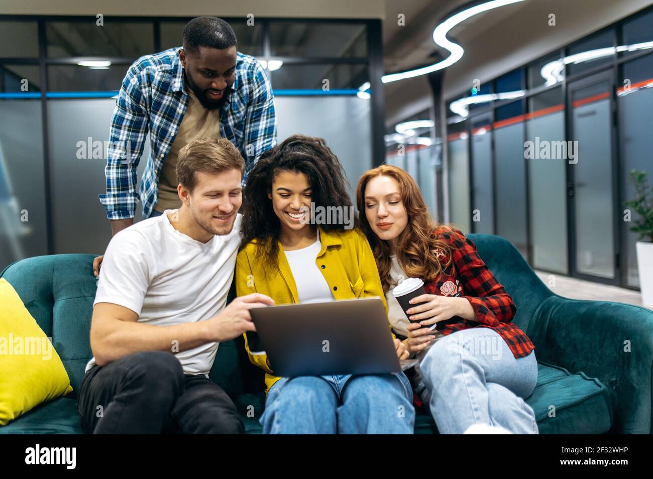 Junge Erwachsene fröhliche Mitarbeiter verwenden Laptop, sitzen auf dem Sofa während der Pause, lustige Videos oder Fotos zu sehen. Glückliche multiethnische Mitarbeiter im Internet surfen, lächeln, Ideen für ein Projekt suchen Stockfoto