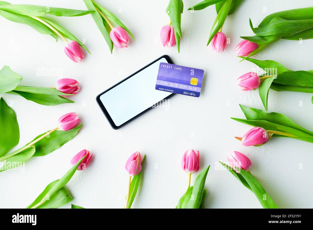 Spring Flat Lay mit Kreditkarte, Tulpen und Smartphone isoliert auf weißem Hintergrund. Stockfoto
