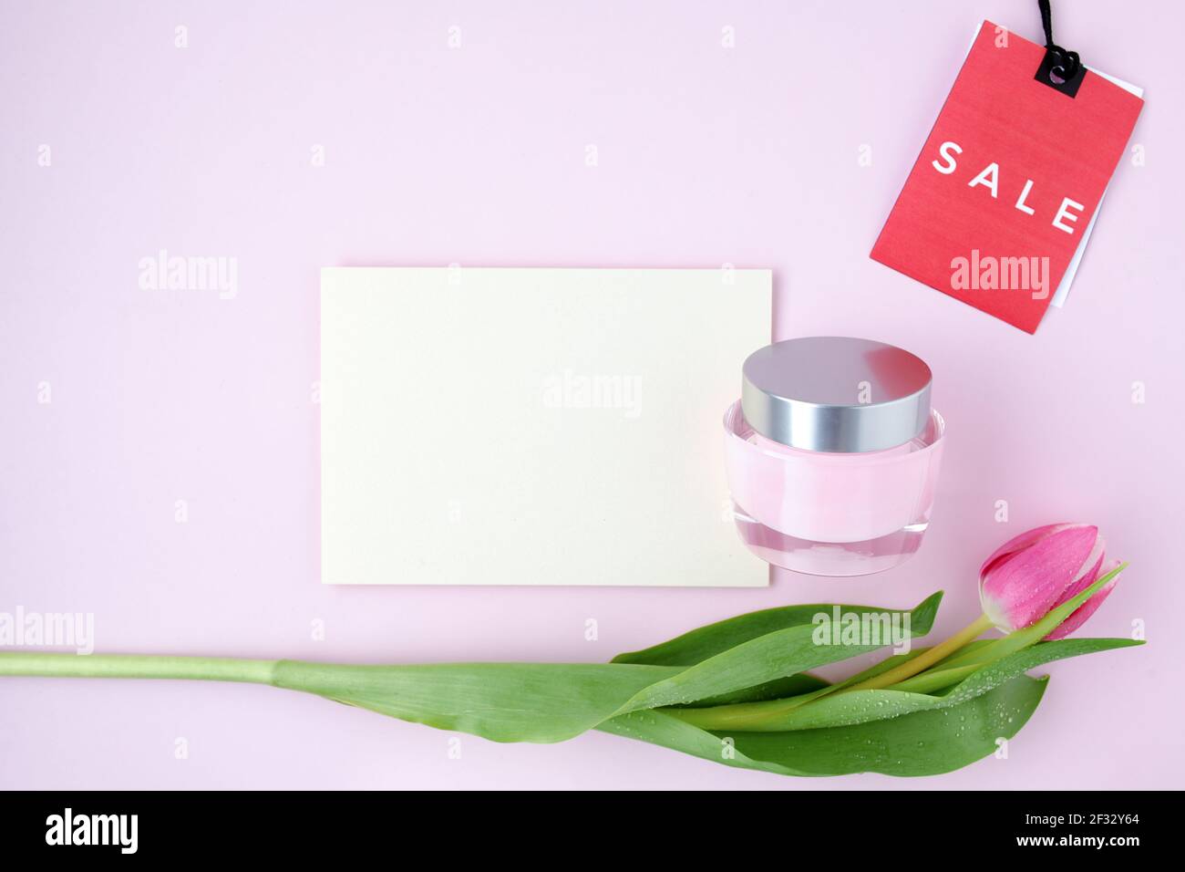 Spring Flat Lay mit Tulpe, Verkaufsetikett, Papierbogen und Gesichtscreme isoliert auf rosa Hintergrund. Stockfoto
