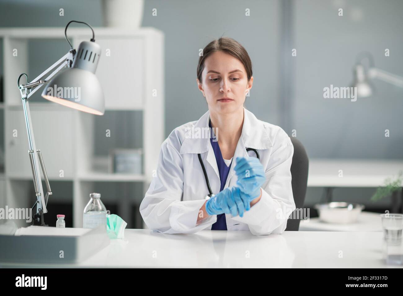 Portrait einer niedlichen Ärztin in blauen medizinischen Latexhandschuhen am Tisch, für die Aufnahme von Patienten. Ein vertrauenswürdiges Gesicht und ein gepflegtes Aussehen Stockfoto