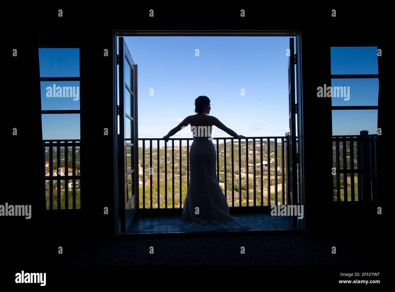 Eine silhouettierte Braut steht vor ihrer Hochzeit auf einem Balkon in ihrem Hochzeitskleid. Stockfoto