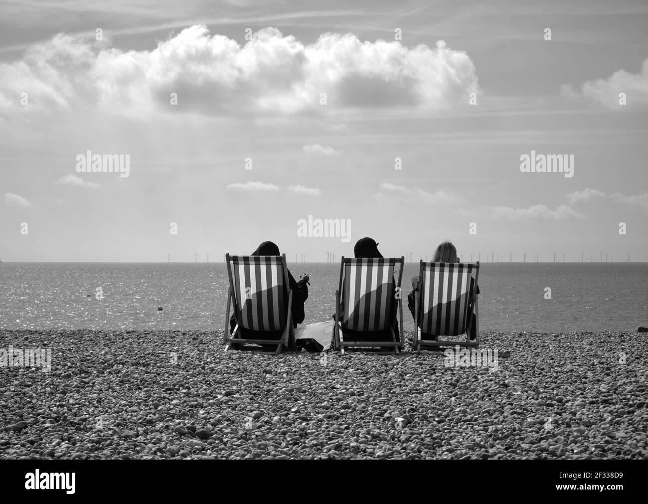 Blick von hinten auf drei Frauen, die auf Strandstühlen sitzen Am felsigen Strand Stockfoto