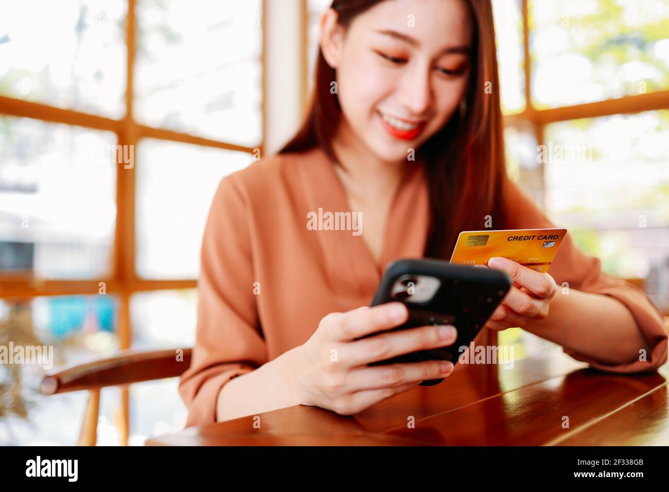 Schöne junge asiatische Frau hält Bank Kreditkarte für die Zahlung Auf dem Smartphone für Online-Shopping sitzen im Café und warten Für Kaffee Stockfoto