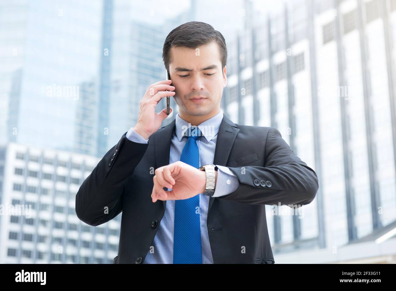 Geschäftsmann, der seine Uhr ansieht, während er anruft, um die Zeit zu überprüfen Handy mit ernsthafteren Gesicht Stockfoto