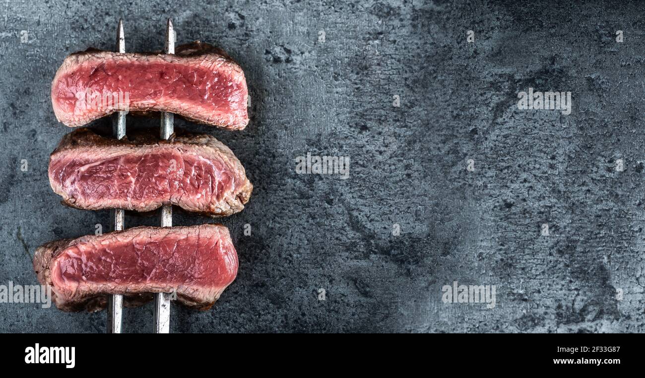 Schiefe Rindersteaks, die auf heißen dunklen Steinen von oben betrachtet zubereitet werden. Stockfoto