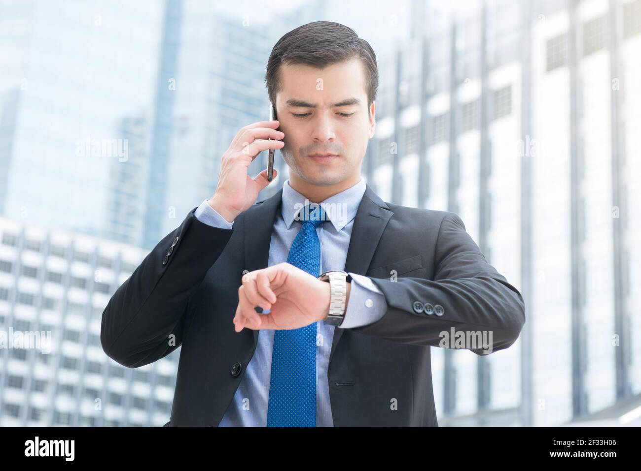 Geschäftsmann, der seine Uhr ansieht, während er anruft, um die Zeit zu überprüfen Handy mit ernsthafteren Gesicht Stockfoto