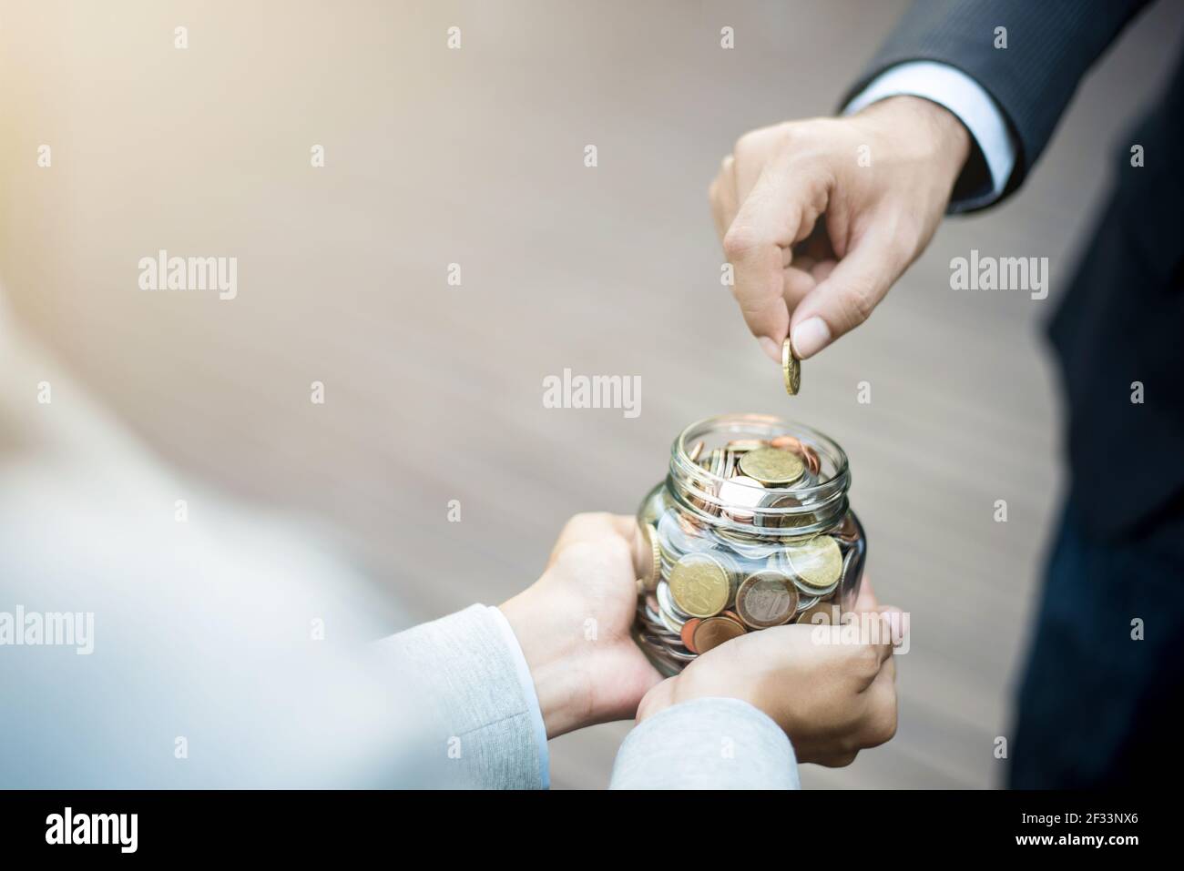 Geschäftsmann Hand Putting Geld (Münze) in das Glas gehalten Von einer Frau Stockfoto