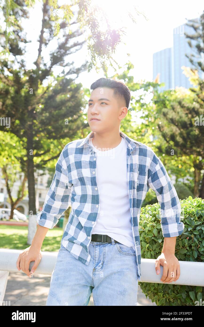Asiatische junge Mann in lässiger Kleidung im Freien in der stehen Stadt in sonnigen Tag Stockfoto