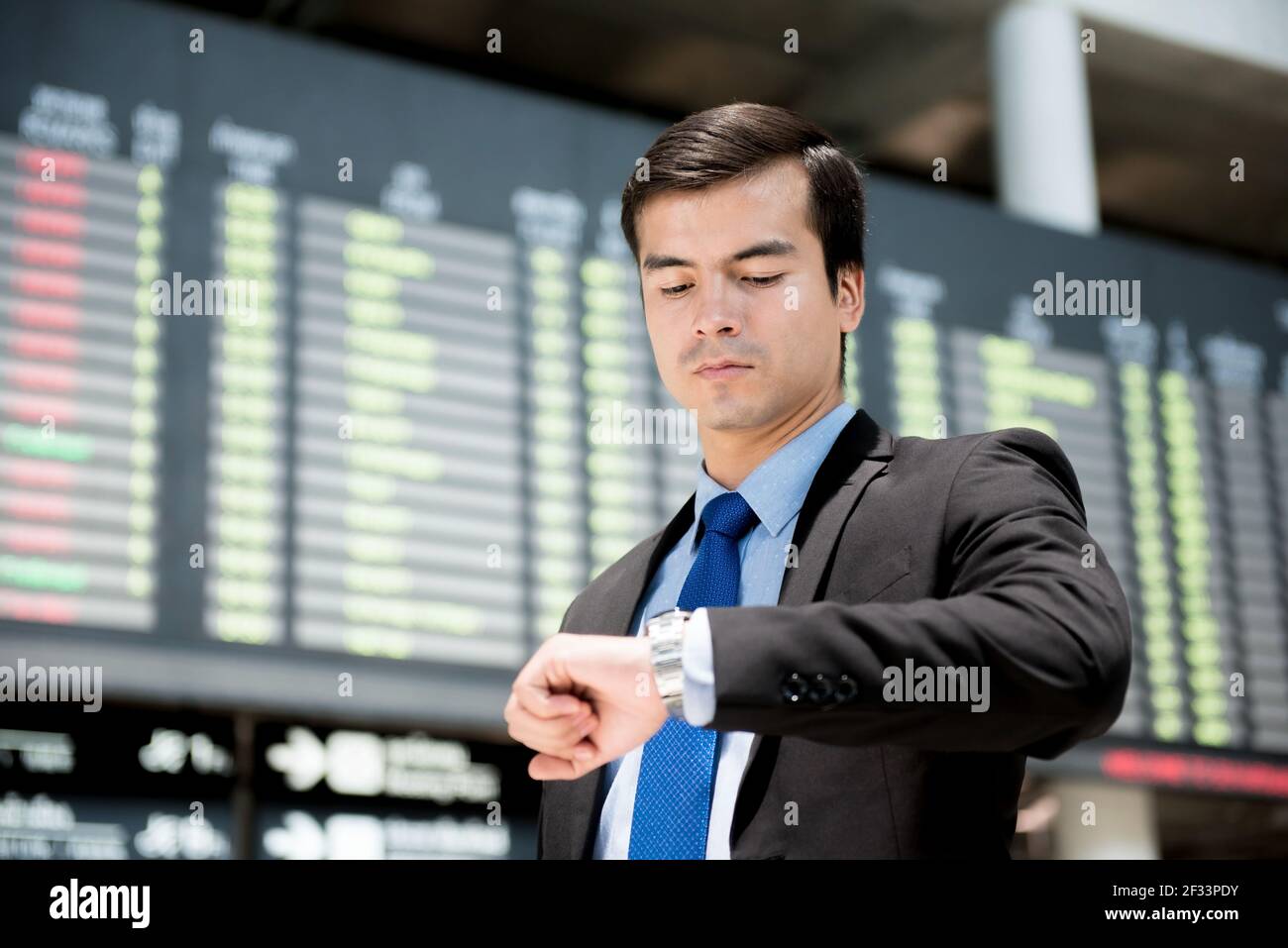Geschäftsmann, der seine Uhr vor dem Flugplan des Flughafens anschaut Am Flughafenterminal Stockfoto