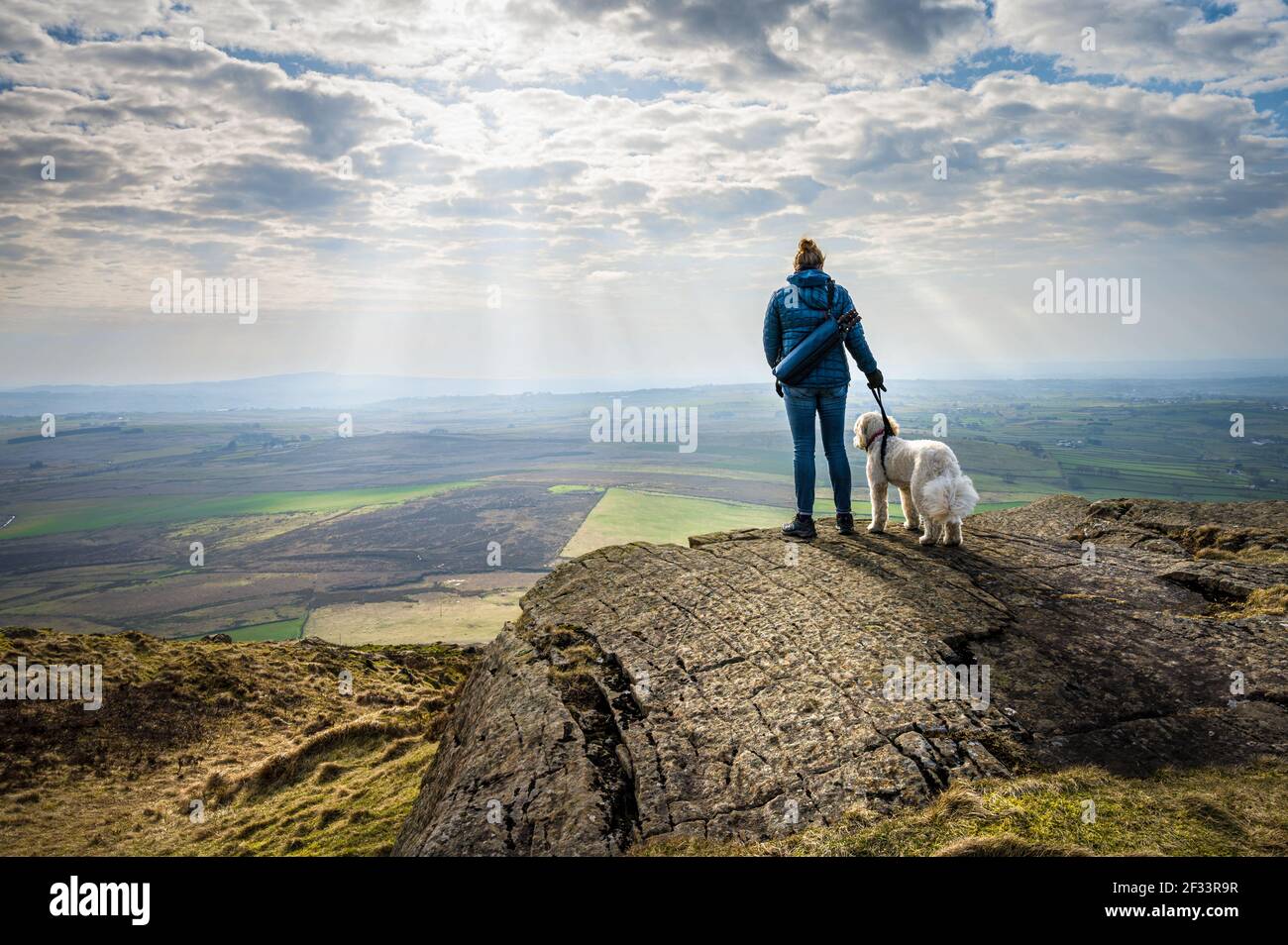 Eine Frau und ihr weißer Hund genießen die Aussicht auf Die irische Landschaft nach dem Klettern auf dem Slemish Mountain in Nordirland Stockfoto
